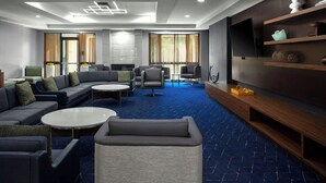 Een moderne hotel lobby met een blauw tapijt, grijze banken, een flatscreen televisie en houten planken.