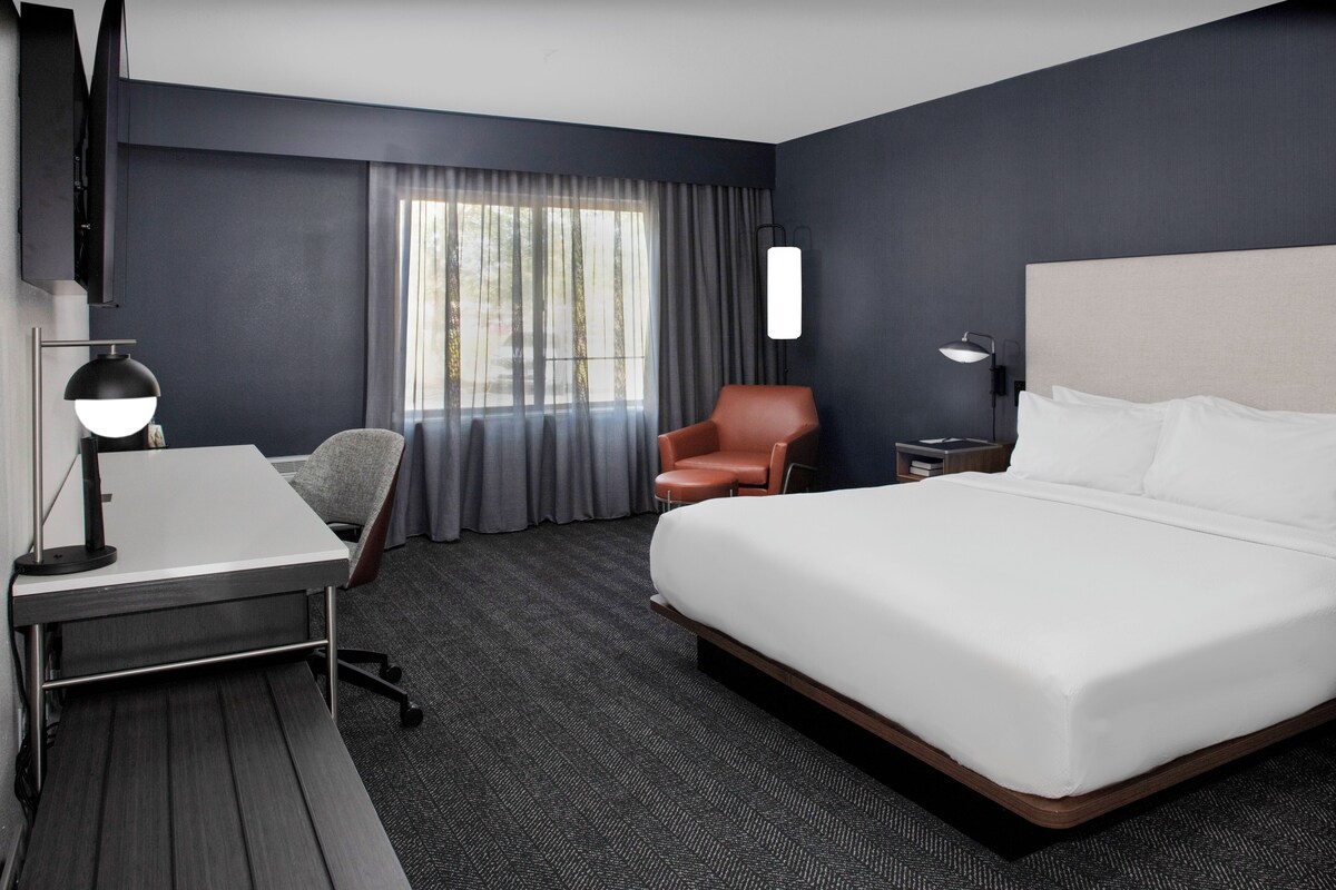 Hotelkamer met een groot bed, een bureau met lamp, een stoel, een nachtkastje en een aan de muur bevestigde televisie.