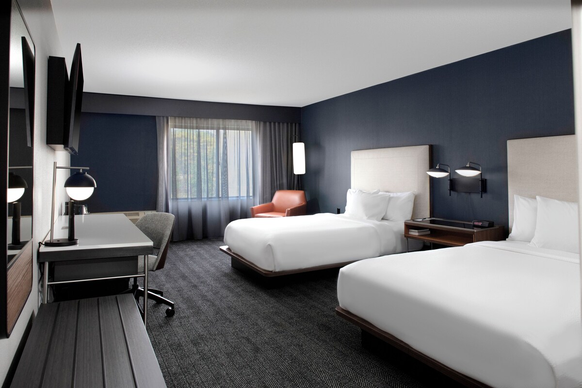 Een hotelkamer met twee bedden, een bureau, een stoel, een televisie en een raam met gordijnen.