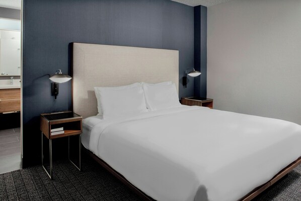 A neatly made bed with a headboard, two bedside tables with lamps, and a dark blue wall. - Courtyard by Marriott Richmond Northwest (Richmond)