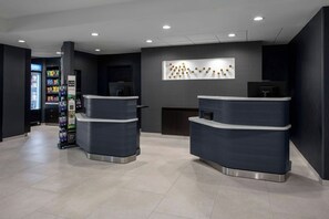 A reception area with two reception desks, a wall-mounted light fixture, and a vending machine. - Courtyard by Marriott Richmond Northwest (Richmond)