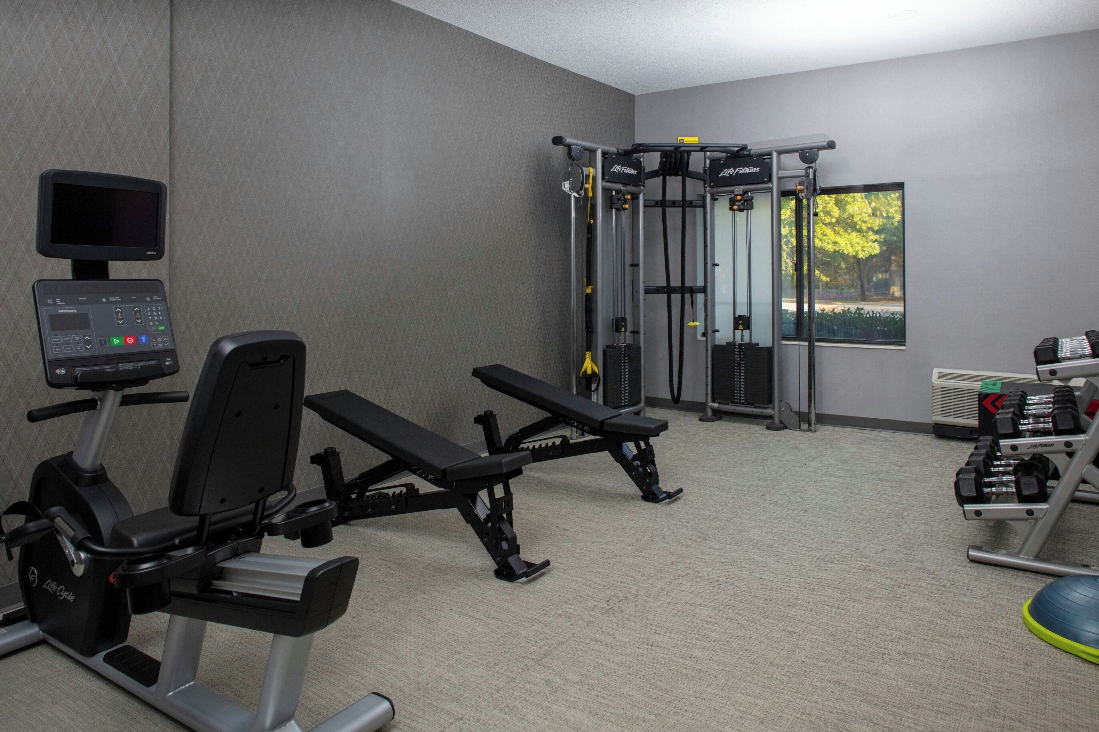 A gym with cardio equipment, weight benches, and a wall-mounted TV.