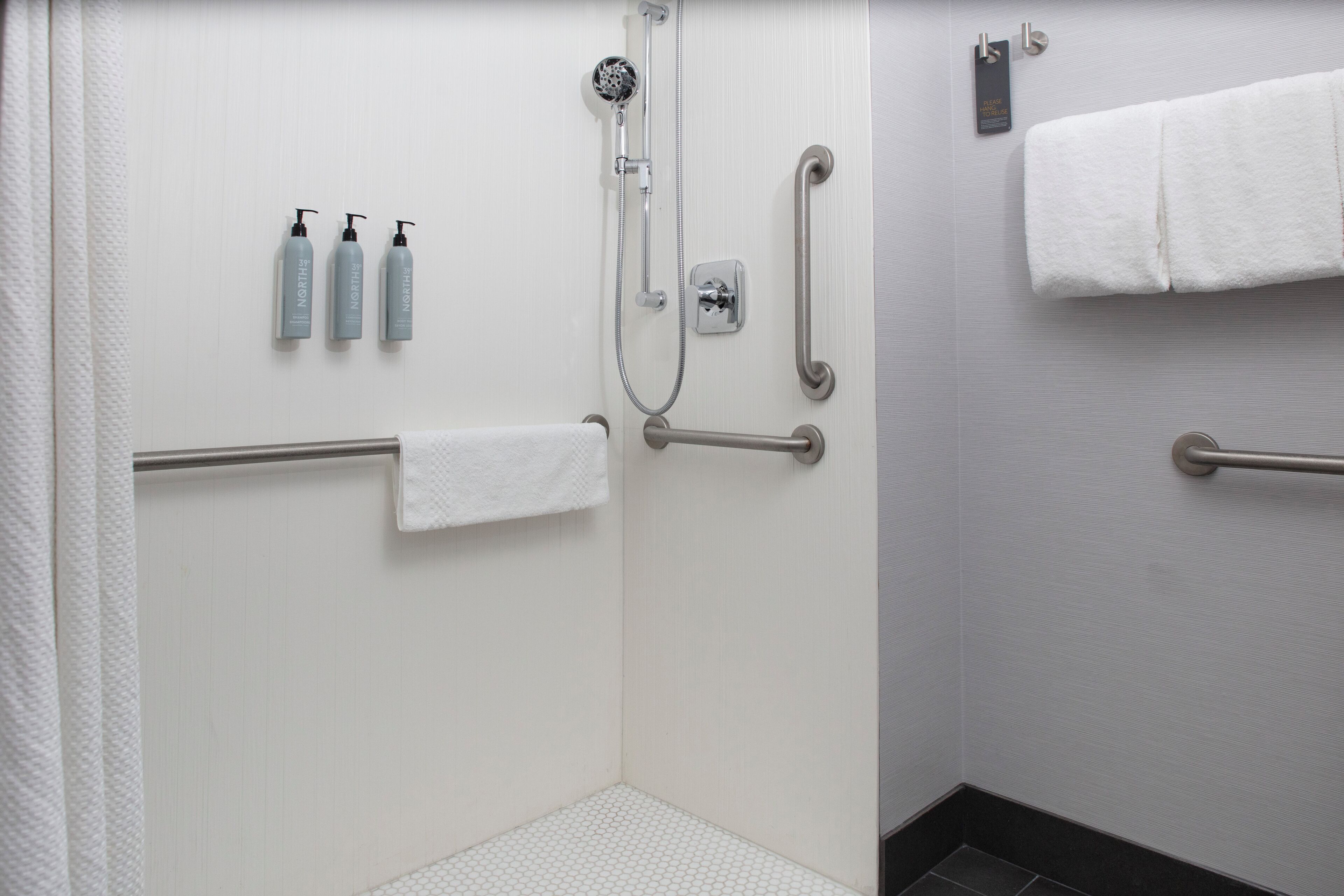 A bathroom with a shower, grab bars, and three bottles of shampoo.