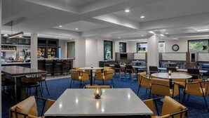 Een modern restaurant met hoge tafels en stoelen, een bar en grote ramen.