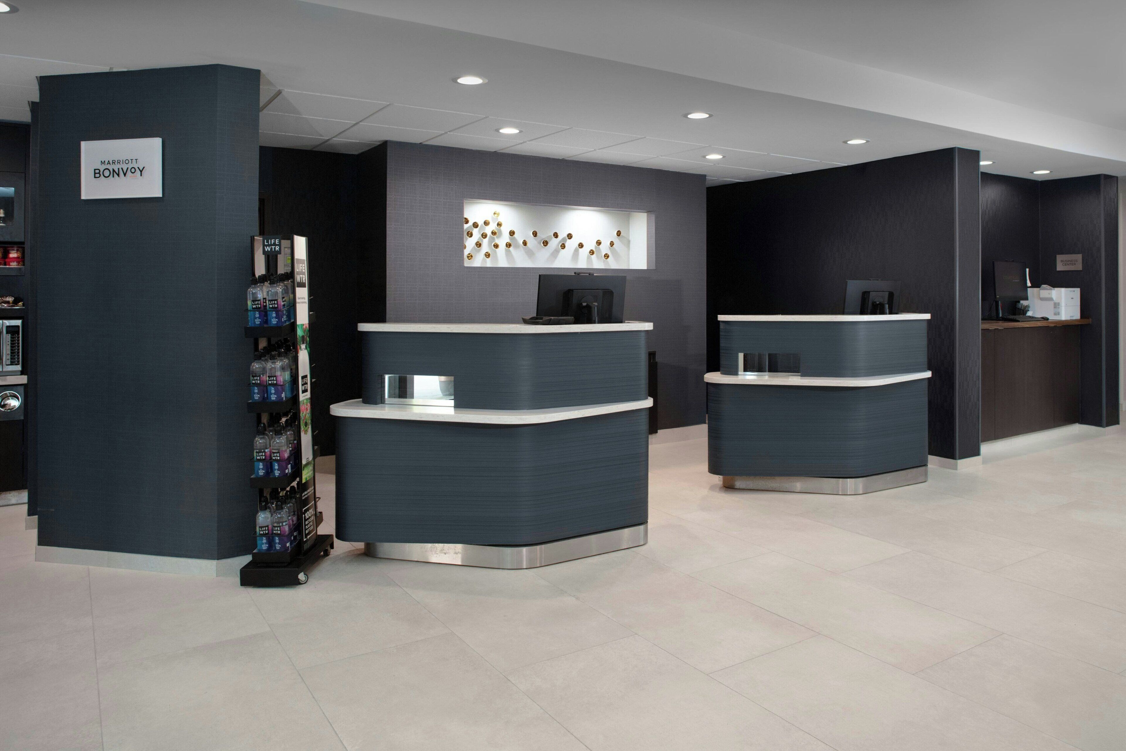 A modern hotel reception area with two reception desks, a vending machine, and a wall-mounted coffee machine.