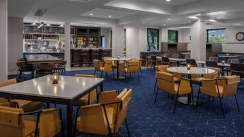 A modern restaurant with multiple seating areas, including round tables and booths, and a bar area with a menu display.