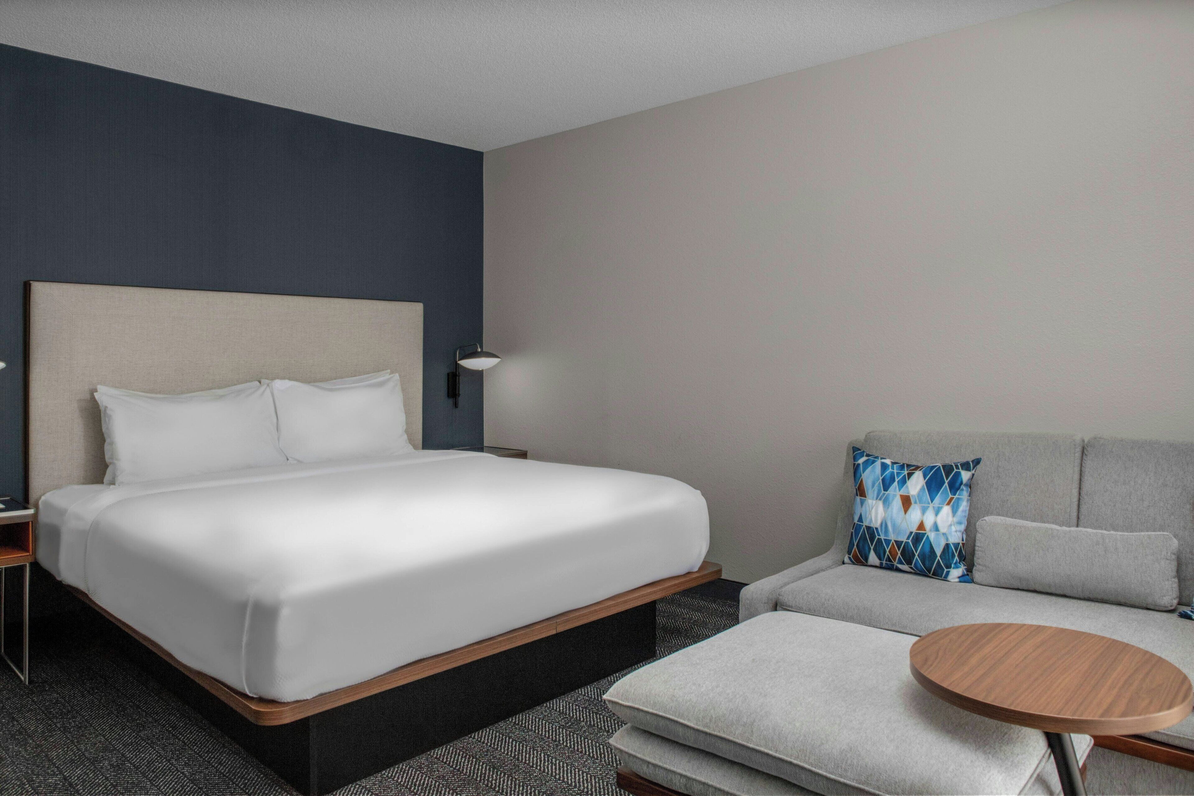 Una habitación de hotel con una cama grande, un sofá, una mesita y una lámpara.