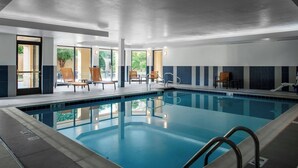 Een zwembad met helderblauw water, omringd door ligbedden en een betegelde vloer.