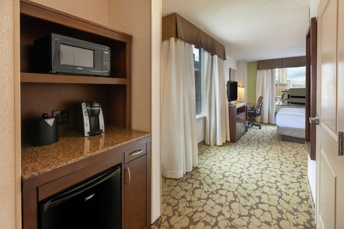 A hotel room with a microwave, coffee maker, and a desk with a chair.