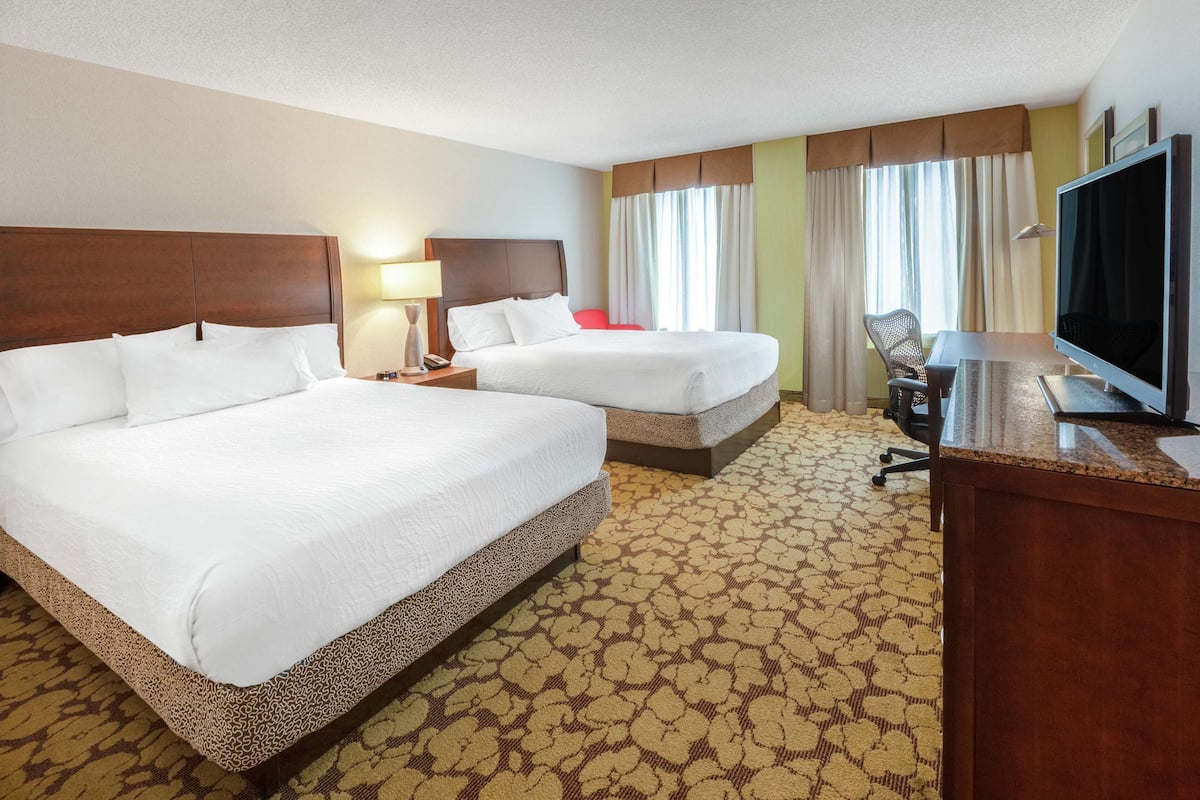 A hotel room with two beds, a desk, a television, and a chair.