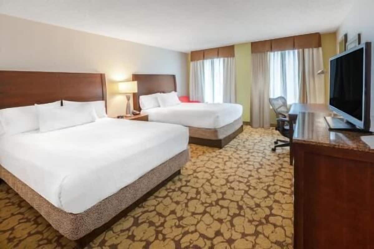 A hotel room with two beds, a desk, a television, and a patterned carpet.