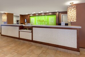 A hotel reception area with a modern design, featuring a reception desk, a green decorative wall, and two pendant lights. - Hilton Garden Inn Pittsburgh University Place (Pittsburgh)