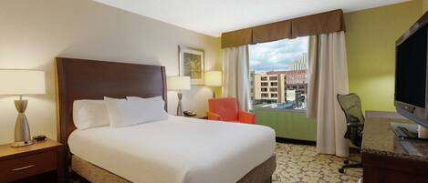 A hotel room with a large bed, a desk, a chair, and a TV.