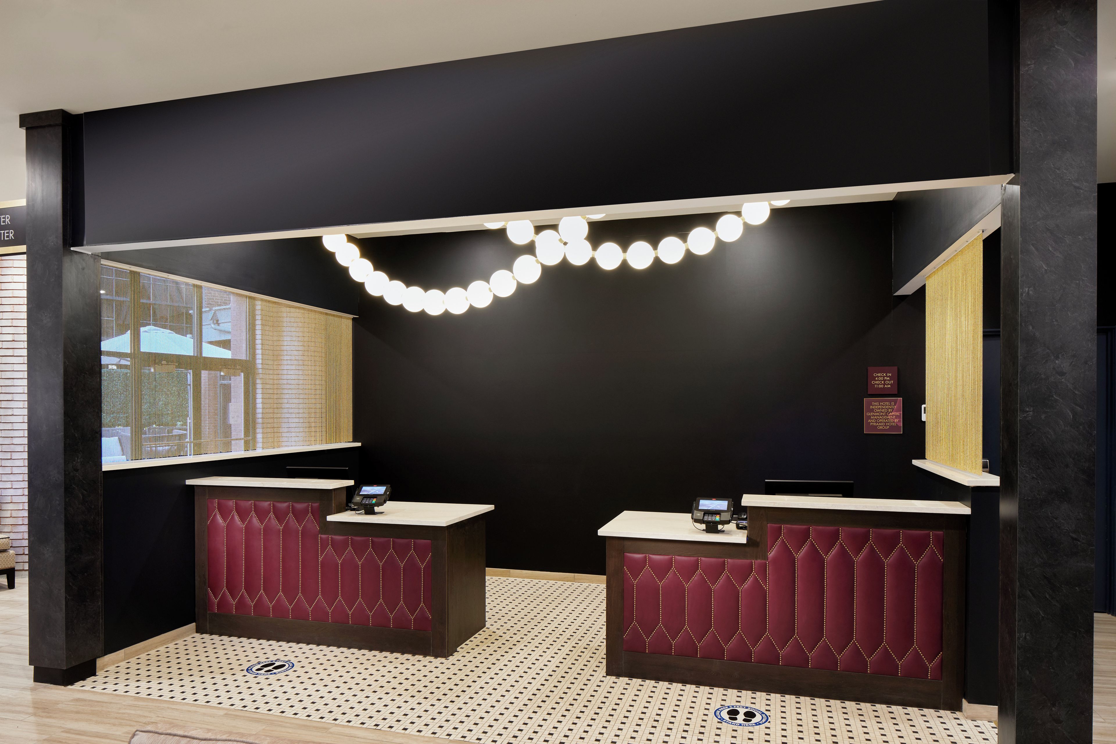 A hotel reception area with two counters, a large window, and a decorative light fixture.