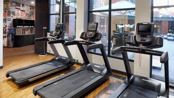 Une salle de sport équipée de trois tapis de course, dotée d’un plancher en bois et de grandes fenêtres.