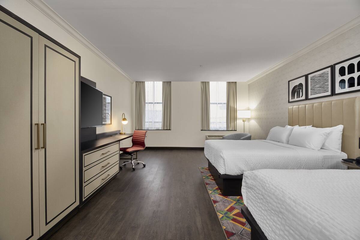 A hotel room with a bed, a desk, a chair, a TV, and a window.
