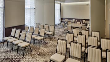 A conference room with rows of chairs and a large table, carpeted floor, and large windows with blinds.