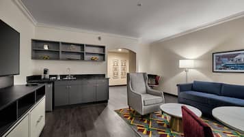 A modern kitchen with dark cabinetry, a built-in coffee machine, and a dining area with a round table and a colorful rug.