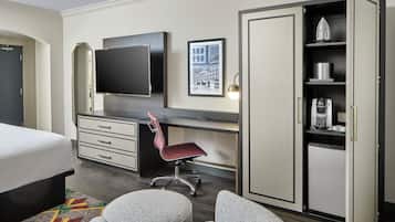 A hotel room with a bed, a desk with a chair, a television, a wardrobe, and a coffee machine.