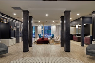 Un hall de hotel con mostrador de recepción, zona de estar y vistas a la ciudad a través de amplios ventanales.