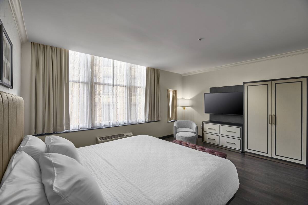 A hotel room with a large bed, a desk, a chair, a wardrobe, and a TV.