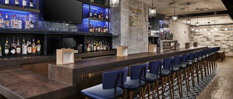 A bar area with a long counter, multiple shelves of bottles, and a seating area with blue chairs.