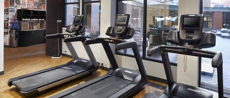 Three treadmill machines in a gym with large windows and a brick wall.