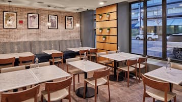 A restaurant interior with brick walls, framed pictures, and a view of the street outside.