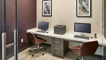 A modern office space with two desks, two chairs, two monitors, a printer, and framed pictures on the wall.