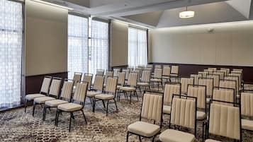 Un salón de conferencias con filas de sillas, ventanas amplias y una alfombra estampada.
