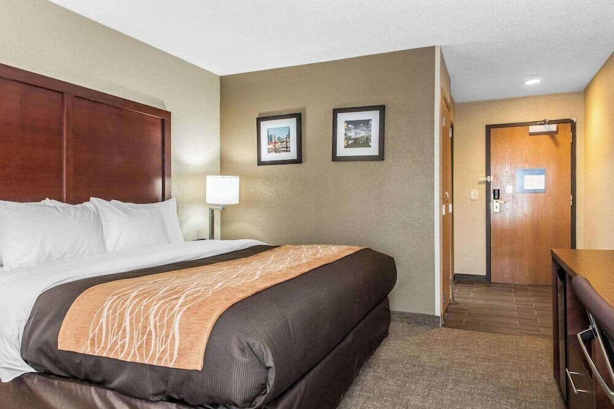 A hotel room with a large bed, a desk, and a door leading to the hallway.