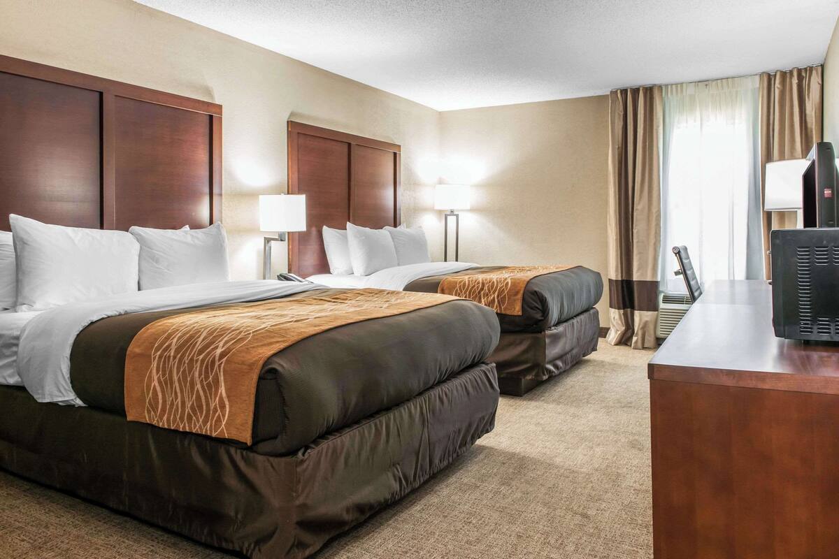 A hotel room with two beds, a desk, and a television.