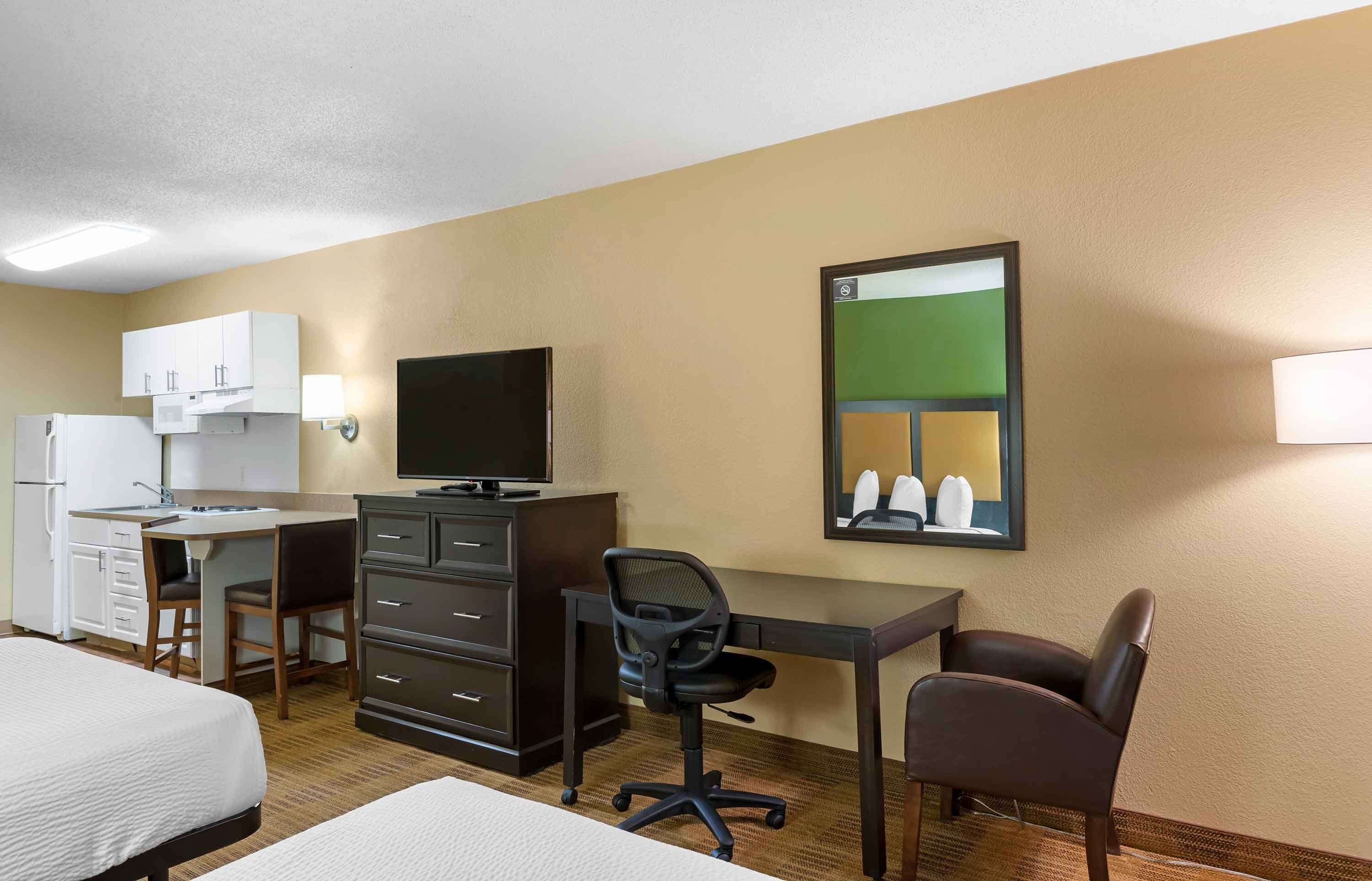 Habitación de hotel con cama, escritorio con computadora, silla, televisor, armario y espejo.