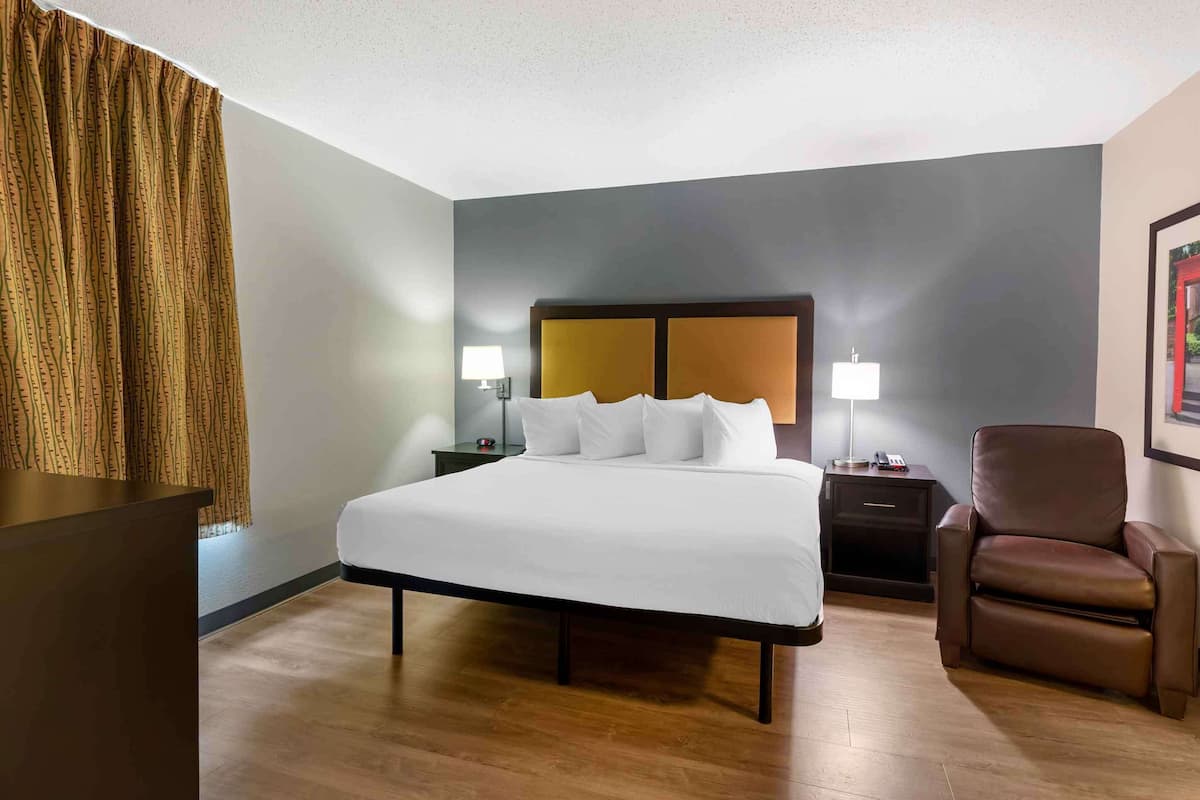 A hotel room with a large bed, two bedside tables with lamps, a brown leather chair, and a curtain.