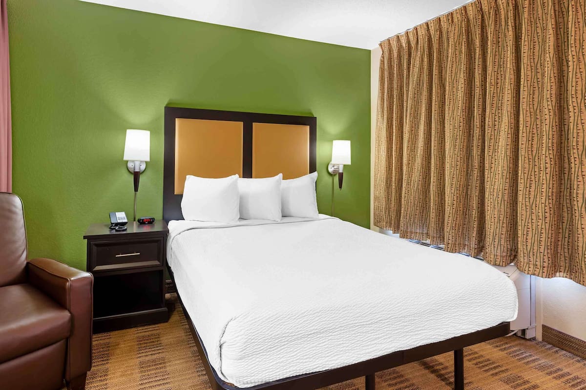 A hotel room with a large bed, two bedside lamps, a nightstand with a phone, and a brown leather chair.