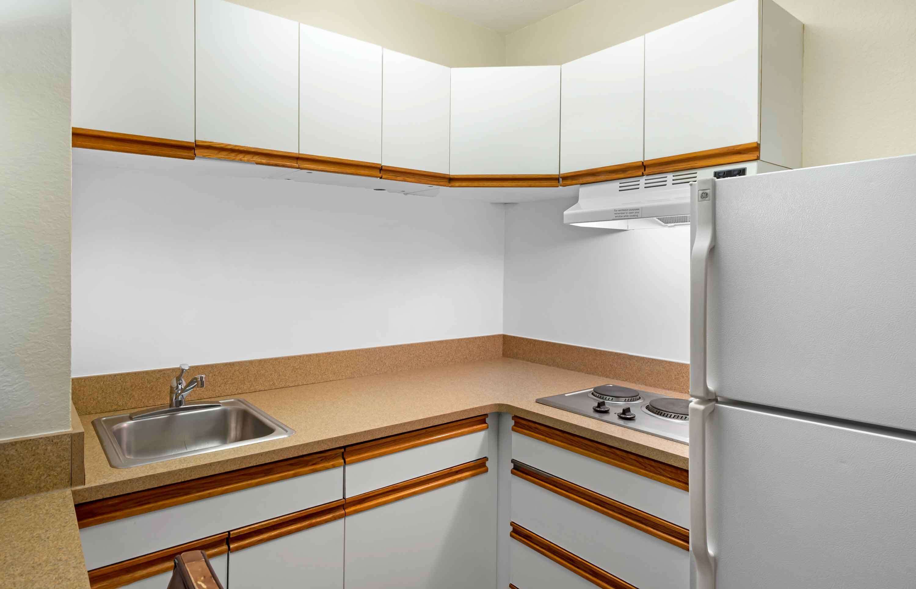 Una cucina compatta con mobili bianchi, un lavello in acciaio inossidabile e un frigorifero integrato.