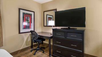 A hotel room with a bed, a desk with a chair, a television, and a dresser.