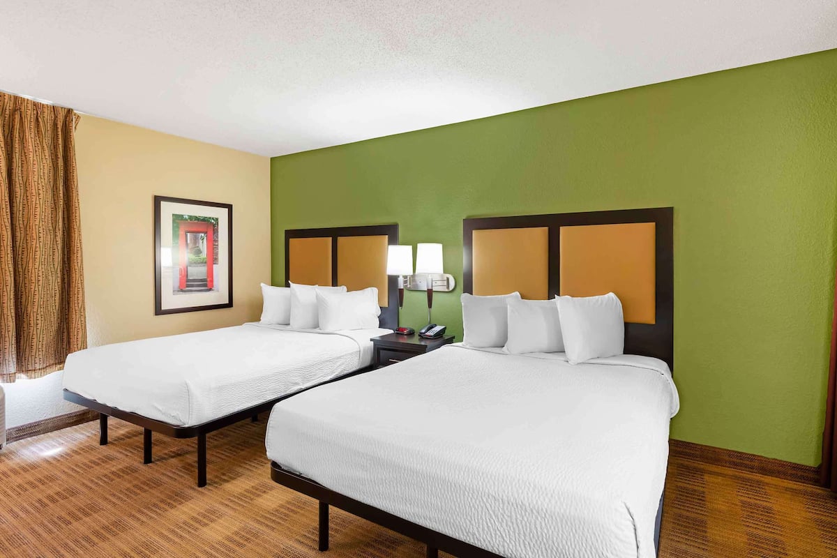 A hotel room with two beds, a nightstand with a lamp, and a framed picture on the wall.