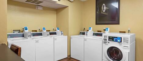 A laundry room with four washing machines and dryers, a table, and chairs.