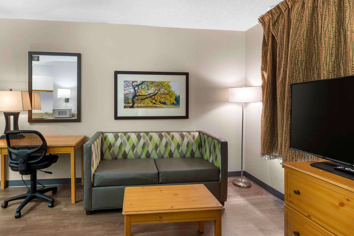 A hotel room with a sofa, a desk with a chair, a television, a lamp, and a framed picture on the wall.