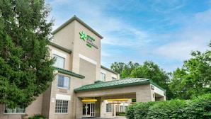 A Stay America hotel with a brick facade, green roof, and a sign indicating a pharmacy. - Extended Stay America Suites North Chesterfield Arboretum (Richmond)
