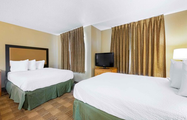 Una habitación de hotel con dos camas, un televisor y cortinas.