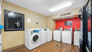 A laundry facility with multiple washing machines and dryers, a red wall, and a ceiling light.