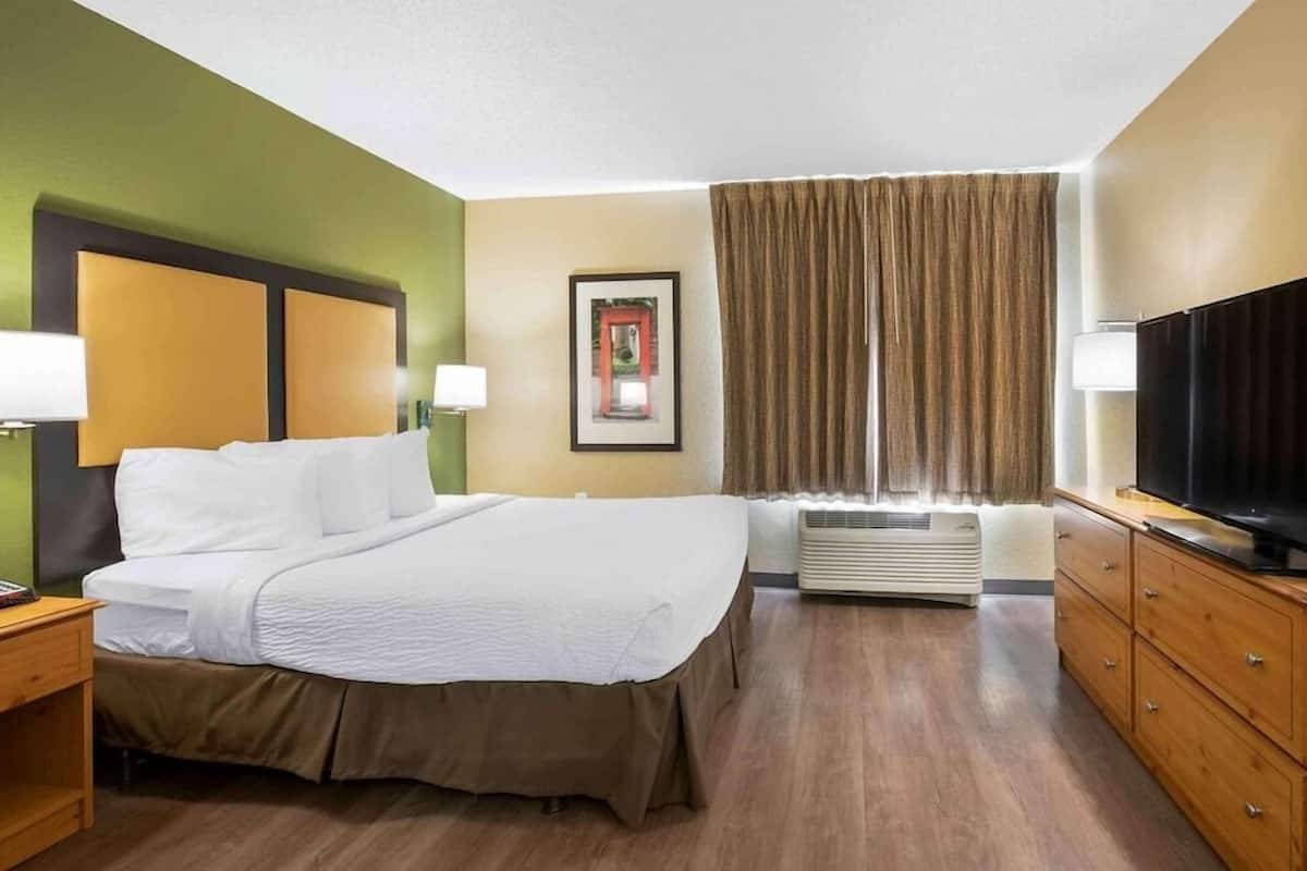 A hotel room with a bed, a television, a desk, and a window with curtains.