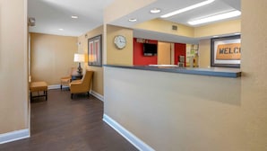 A hotel reception area with a clock, a welcome sign, and a seating area with a lamp.