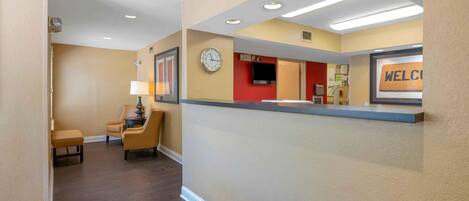 A hotel reception area with a clock, a welcome sign, and a seating area with a lamp.