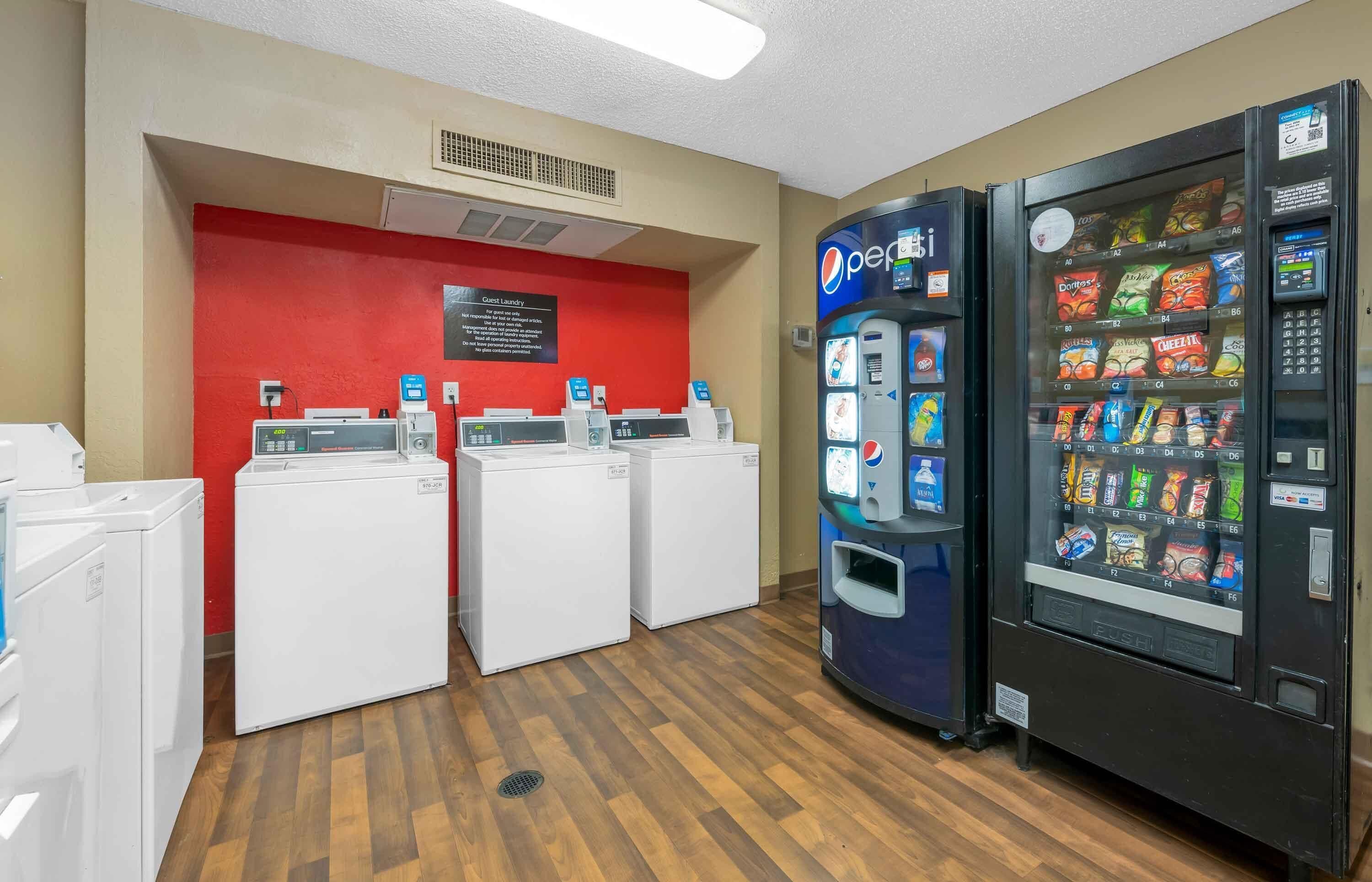 A laundry area with three washing machines and a vending machine with snacks.