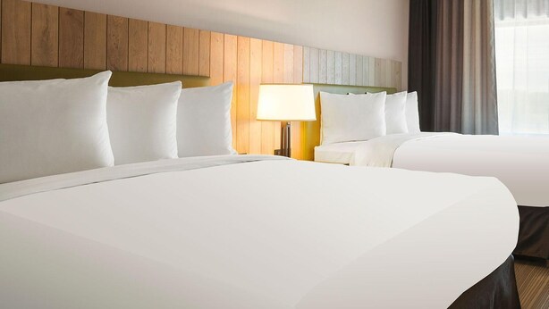 A hotel room with two beds, a wooden headboard, a bedside lamp, and a window with curtains. - Country Inn & Suites by Radisson, Mishawaka - South Bend (Mishawaka)