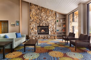 A living room with a stone fireplace, a sofa, a coffee table, and a patterned carpet. - Country Inn & Suites by Radisson, Mishawaka - South Bend (Mishawaka)