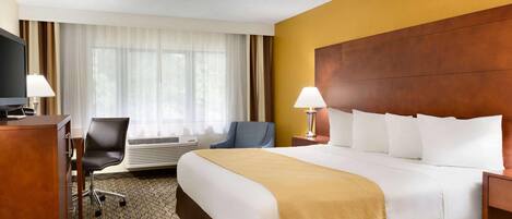 Ein Hotelzimmer mit einem großen Bett, einem Schreibtisch mit Computer, einem Stuhl und einem Fernseher.